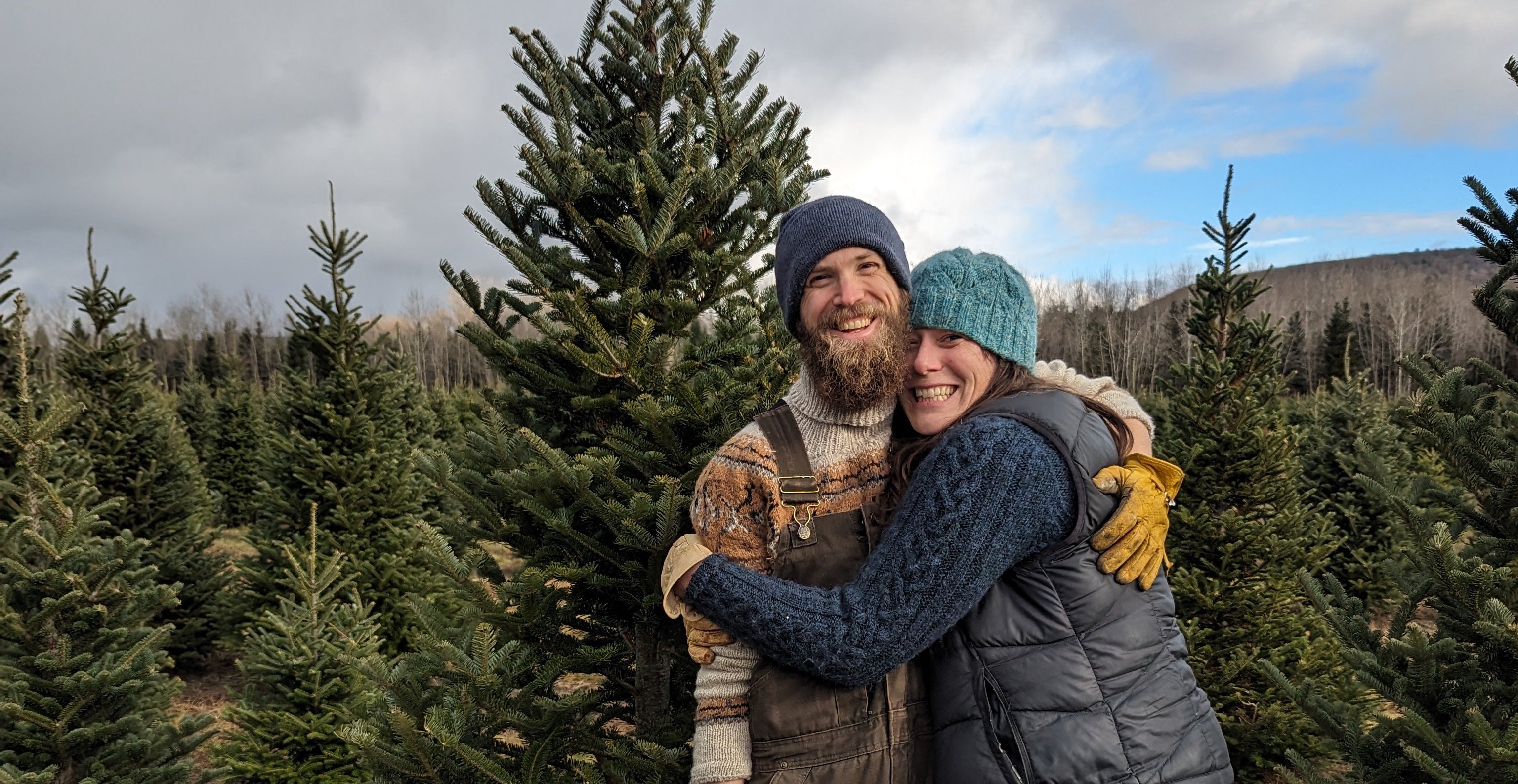 Two people hugging in a field of trees on a cloudy day